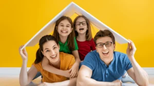 Mladá rodinka s deťmi sa s radosťou schováva pod maketou domčeka. Ich úsmevy vyjadrujú túžbu po vlastnom bývaní a daňový bonus im v tom môže pomôcť.